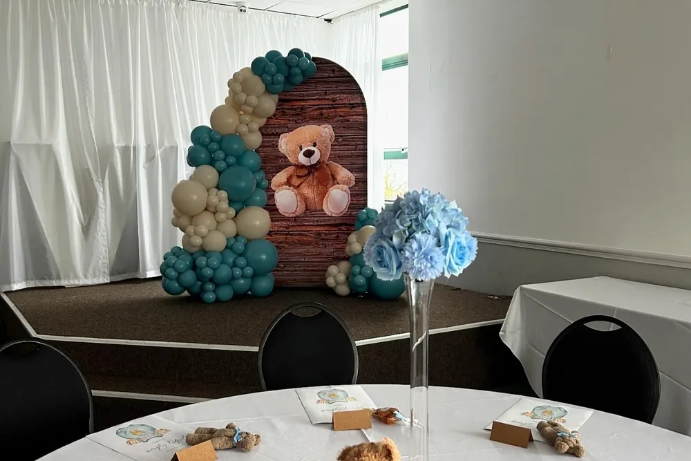 A baby shower set up in the function room with a balloon arch, teddy backdrop and a dressed table