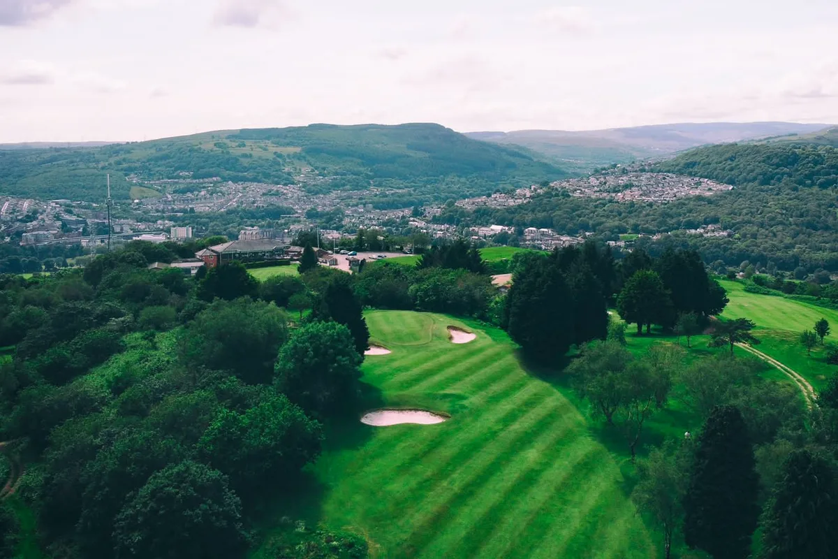 The 5th green from above: tree-lined, bunkered, with the town in the valley behind